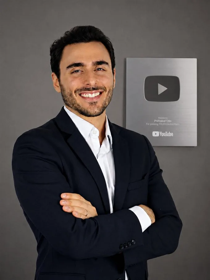 Professor Otto, de terno, ao lado da placa de 100 mil inscritos